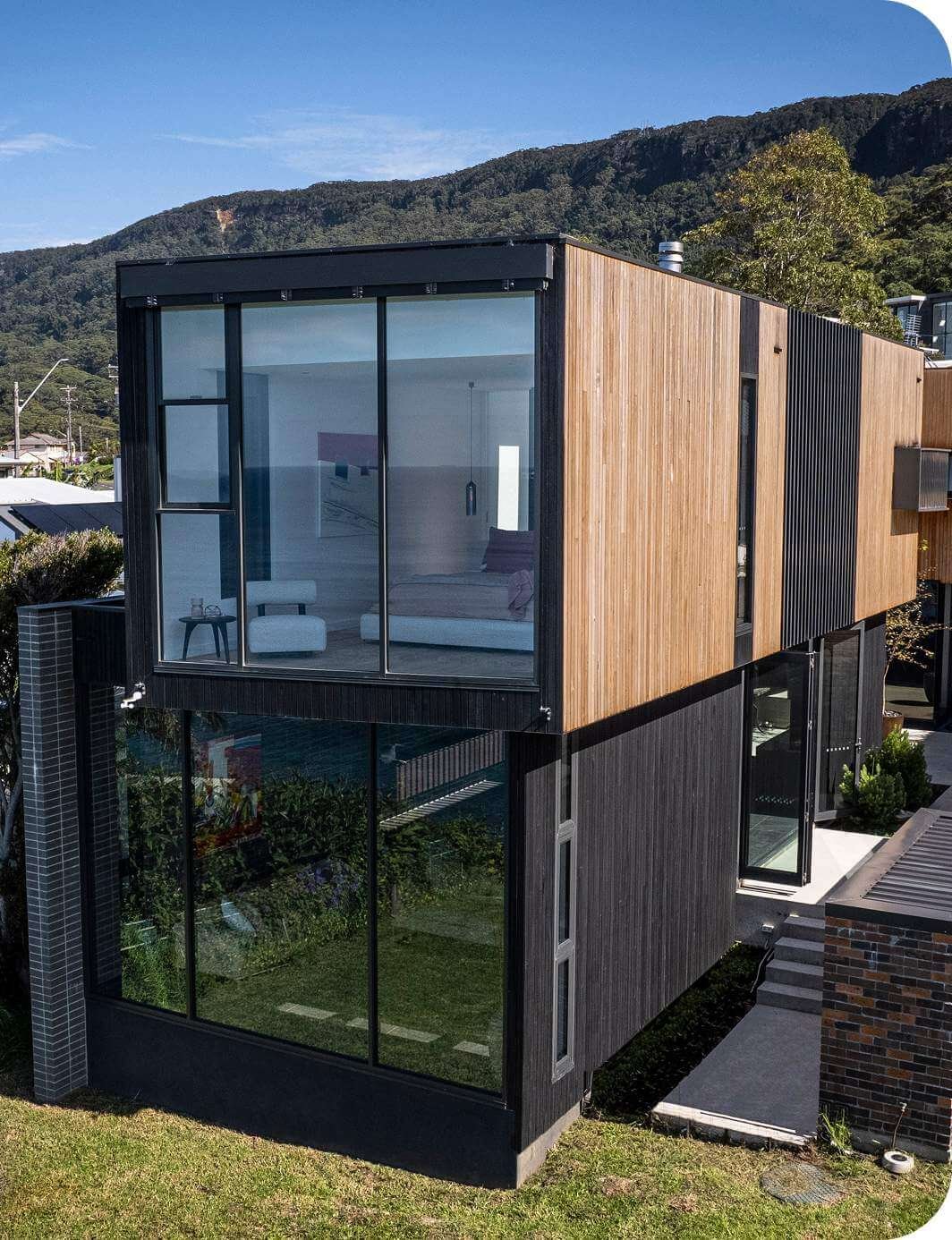 Modern two-storey home with timber cladding and full-height glass windows.