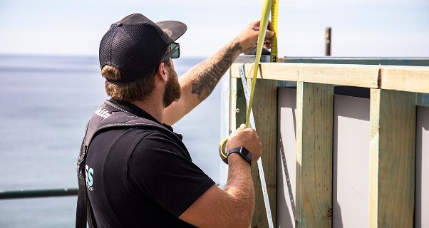 Builder measuring a timber frame with a tape measure by the ocean.
