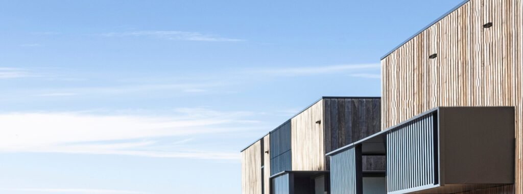 Timber-clad modern townhouses against a clear blue sky.